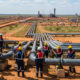 African oil and gas infrastructure under development with workers inspecting pipelines against a backdrop of arid land, symbolizing the continent's untapped energy potential and the need for investment.