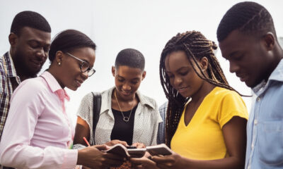A group of diverse, young African professionals collaborates, using a smartphone and notebook, symbolizing Africa's youthful population driving innovation, technology, and economic growth.
