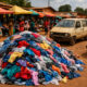 Pile of used clothing and old vehicles at a market in Africa, symbolizing the continent’s role as the world’s unpaid sustainability buffer — representing over $150 billion in unclaimed environmental credits from decades of absorbing Global North waste.