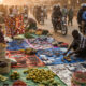 A bustling African street market at dawn, showing vendors setting up stalls, informal traders selling goods, and motorcycle taxis (boda bodas) weaving through the crowd — a vivid representation of Africa’s informal economy thriving beyond GDP metrics.
