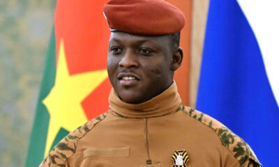 Portrait of Ibrahim Traoré, President of Burkina Faso, in military uniform, standing against a backdrop of the national flag, symbolizing leadership and national resilience in the Sahel region