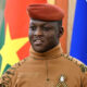 Portrait of Ibrahim Traoré, President of Burkina Faso, in military uniform, standing against a backdrop of the national flag, symbolizing leadership and national resilience in the Sahel region