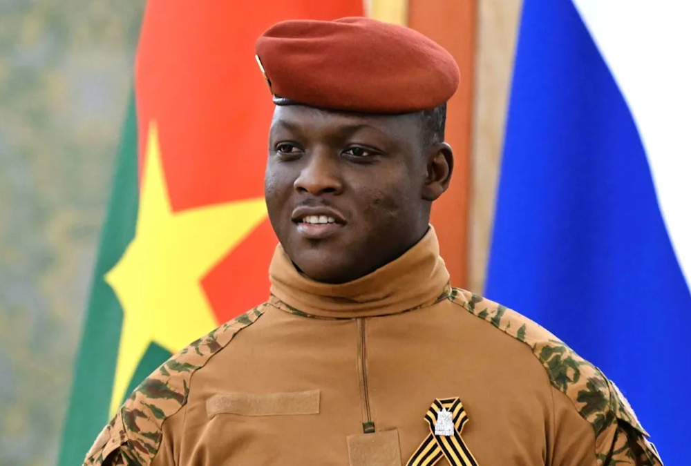 Portrait of Ibrahim Traoré, President of Burkina Faso, in military uniform, standing against a backdrop of the national flag, symbolizing leadership and national resilience in the Sahel region