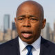 New York City Mayor Eric Adams announcing the end of his reelection campaign, with city skyline in the background.