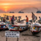Coastal fishing village in West Africa with small wooden boats at sunset, symbolizing traditional artisanal fisheries threatened by industrial foreign fishing fleets and fishmeal exports