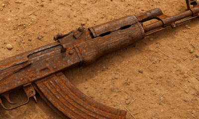A close-up of a rusted Kalashnikov-style rifle (AK-47) lying on dry, dusty ground, symbolizing the widespread proliferation of small arms and conflict in Africa's Sahel region.