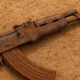A close-up of a rusted Kalashnikov-style rifle (AK-47) lying on dry, dusty ground, symbolizing the widespread proliferation of small arms and conflict in Africa's Sahel region.