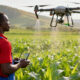 African farmer using a drone for precision agriculture, monitoring crop health, spraying fertilizers, and improving farm yields sustainably.