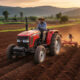 African farmer operating a tractor in a vast cultivated field, symbolizing the urgent need for agricultural mechanization to unlock Africa's farming potential and drive economic transformation.