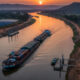 Wide-angle shot of a cargo barge moving along a vast African river at sunset, representing new inland trade routes and infrastructure investment for sustainable continental development.