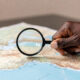 A magnifying glass held over a map of Africa by an African hand, shifting the focus from external to internal analysis.