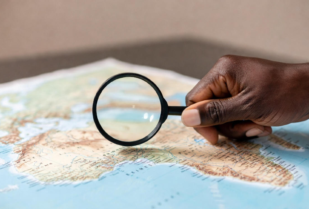 A magnifying glass held over a map of Africa by an African hand, shifting the focus from external to internal analysis.