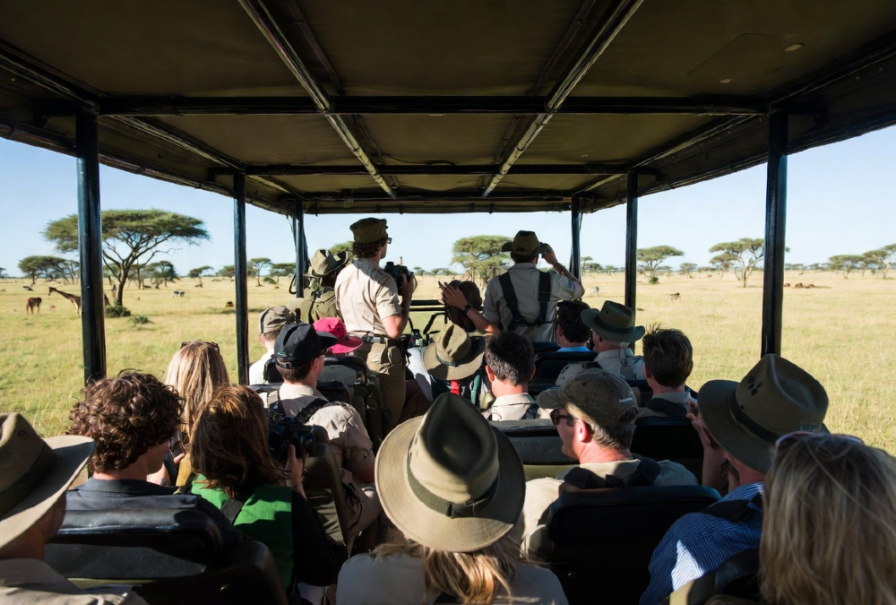 Group of diverse tourists on a safari vehicle viewing wildlife in the Maasai Mara, Kenya.