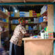 African market trader stocking shelves at a local kiosk, representing relationship-driven last-mile distribution in sub-Saharan Africa where trust and personal connections power commerce more than algorithms or apps.