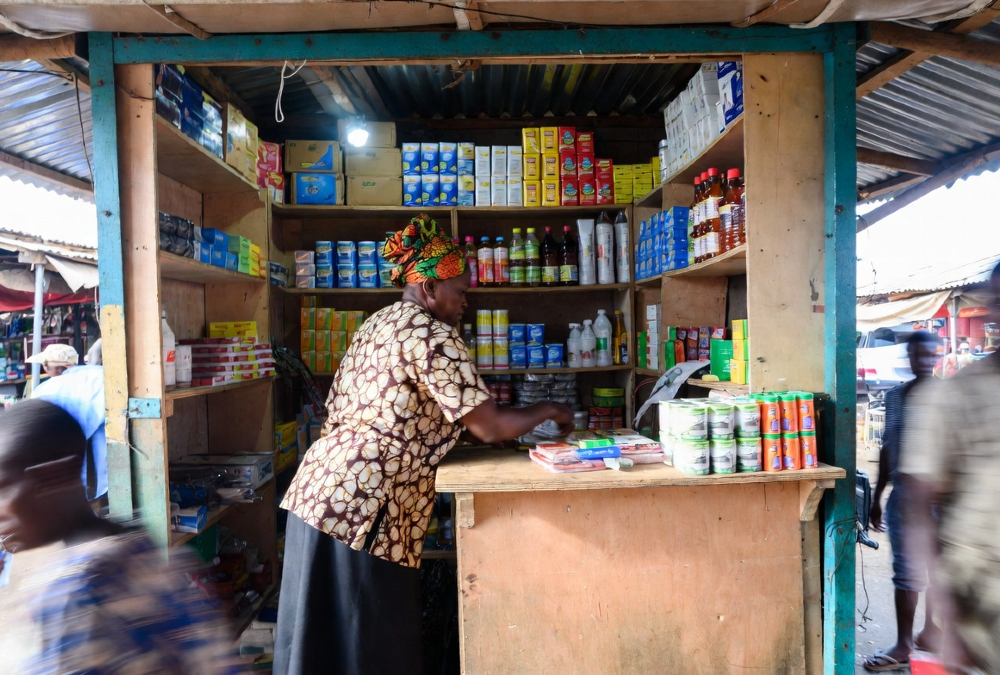 African market trader stocking shelves at a local kiosk, representing relationship-driven last-mile distribution in sub-Saharan Africa where trust and personal connections power commerce more than algorithms or apps.
