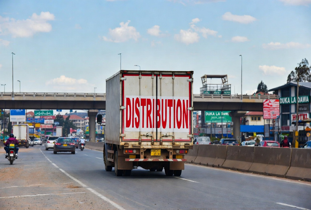 A logistics truck navigating a busy Kenyan market street, representing the challenges and opportunities of distribution strategy for international manufacturers entering the East Africa consumer market.