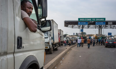 African truck driver waiting at a crowded border crossing with customs booths, symbolizing operational delays and cross-border trade bottlenecks across the continent.