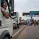African truck driver waiting at a crowded border crossing with customs booths, symbolizing operational delays and cross-border trade bottlenecks across the continent.