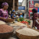 Modern African market scene with fresh traditional foods like millet, sorghum, and vegetables, symbolizing healthy local diets contrasted with urban processed food culture and the impact of Western development on public health