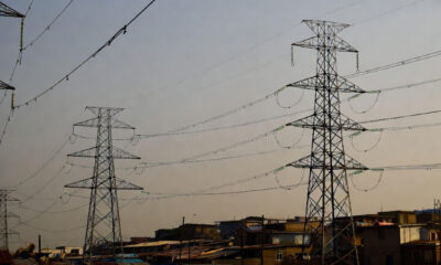High-voltage power lines stretching over informal settlements in Africa and the Caribbean, where homes below remain without electricity, illustrating energy inequality and lack of grid access despite nearby infrastructure