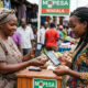 African woman using mobile phone for mobile money payment at a market in Lusaka, Zambia.