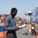 An African export trader reviewing shipment documents at a busy port, with cargo containers and freight vessels in the background, representing China Africa zero-tariff trade opportunities for African nations.