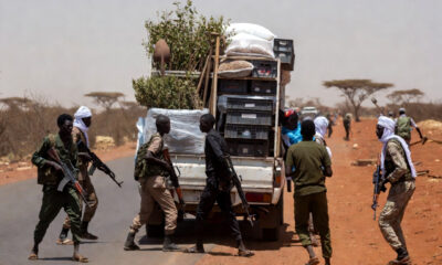 Armed militants on a dusty Sahel road blocking a humanitarian vehicle carrying tree-planting supplies and Ebola response equipment, symbolizing how armed groups obstruct climate and health projects in Africa.