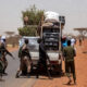 Armed militants on a dusty Sahel road blocking a humanitarian vehicle carrying tree-planting supplies and Ebola response equipment, symbolizing how armed groups obstruct climate and health projects in Africa.