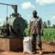 African farmer holding fertilizer bag beside small-scale oil mill, symbolizing agriculture subsidy myths and local industry