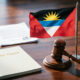 Antigua and Barbuda flag beside a courthouse gavel, symbolizing the nation's sovereign stand on U.S. Third-Country Nationals deportation talks